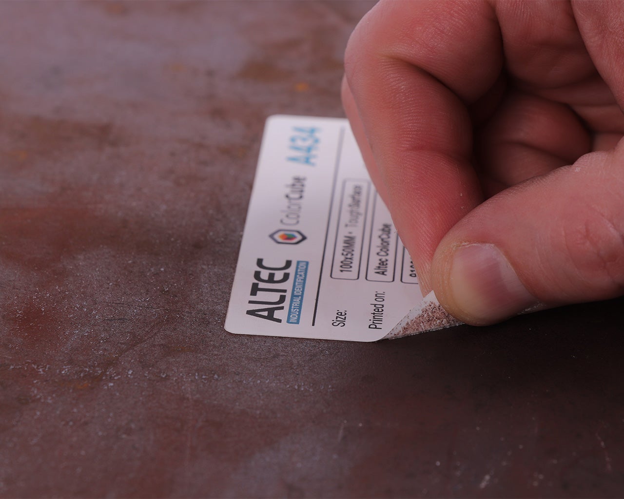 Hand die een full-color label aanbrengt op een ruwe metalen ondergrond