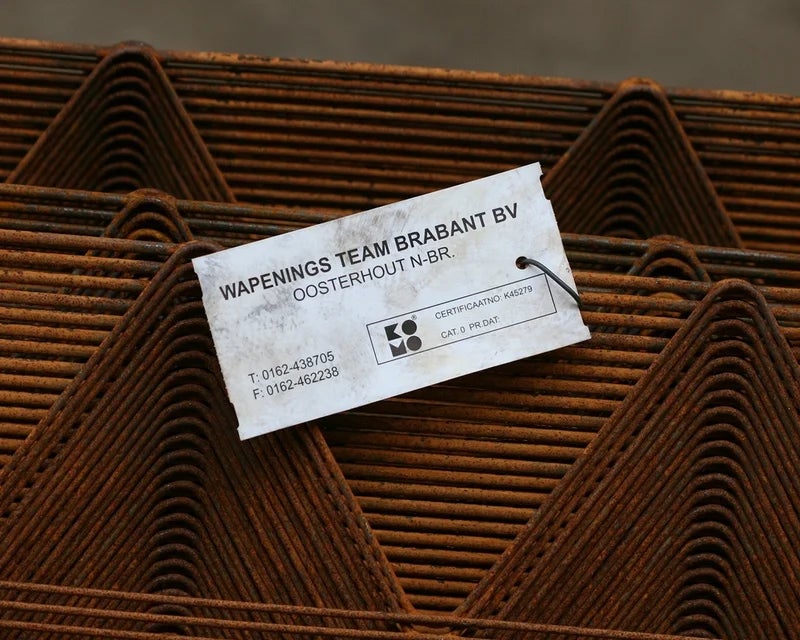 Industriële tag bevestigd aan gestapelde staalprofielen met bedrijfsgegevens en certificaatnummer
