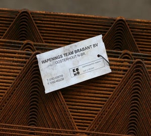 Industriële tag bevestigd aan gestapelde staalprofielen met bedrijfsgegevens en certificaatnummer
