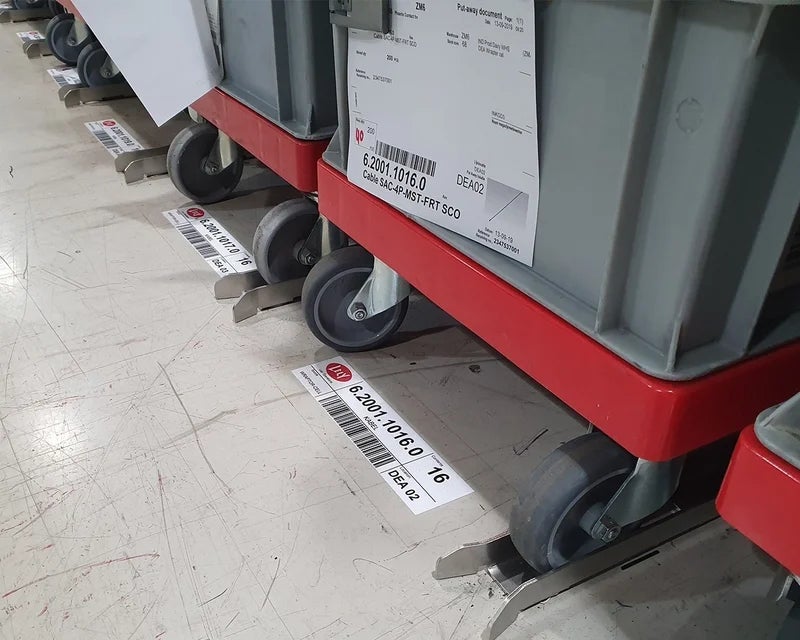 Full-color logistic mat met barcodes en nummers geplaatst bij rolcontainers in logistieke omgeving