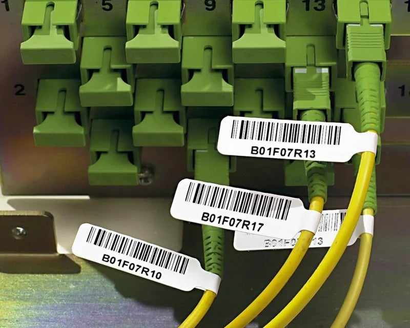 Witte vlaglabels met barcode en identificatiecode op gele glasvezelkabels
