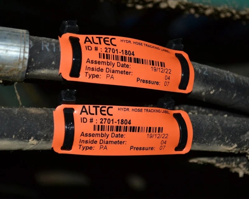 Oranje kabelmerkers met barcode en assemblagedatum op hydraulische slangen