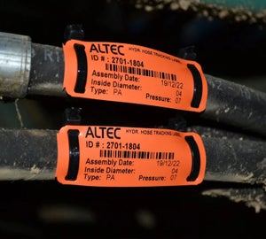 Oranje kabelmerkers met barcode en assemblagedatum op hydraulische slangen