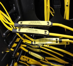 Gele kabelmerkers met unieke codes op glasvezelkabels in datacenter patchkast