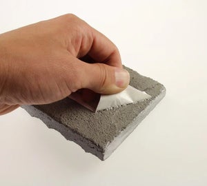 Hand probeert ToughSurface Extreme label van ruw betonnen oppervlak te verwijderen