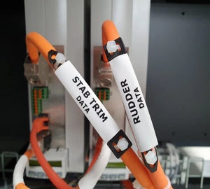 Witte bedrukbare krimpkousen met functieomschrijving op oranje kabels in technische installatie