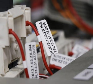 Witte vlaglabels met adercodes op rode aders bij klemmenblokken in schakelkast