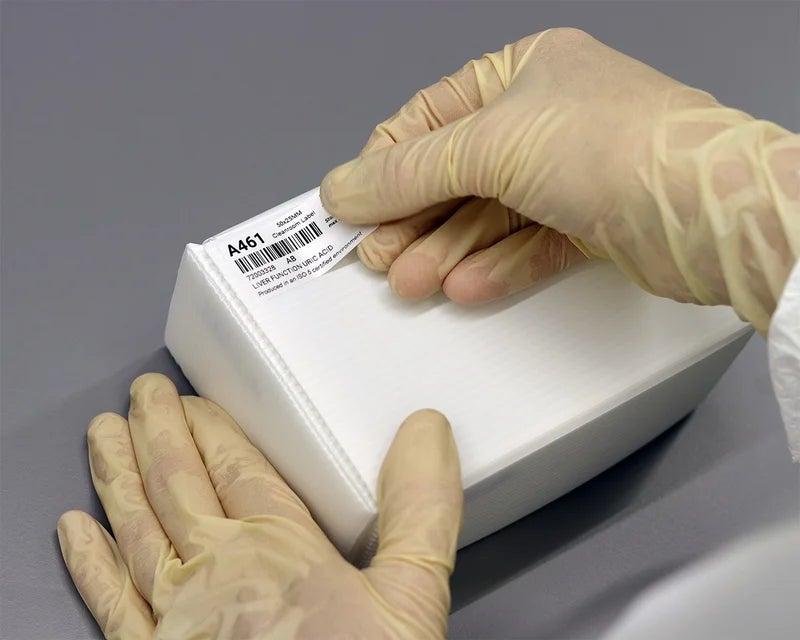 Medewerker brengt cleanroom label met tekst en barcode aan op kunststof doos