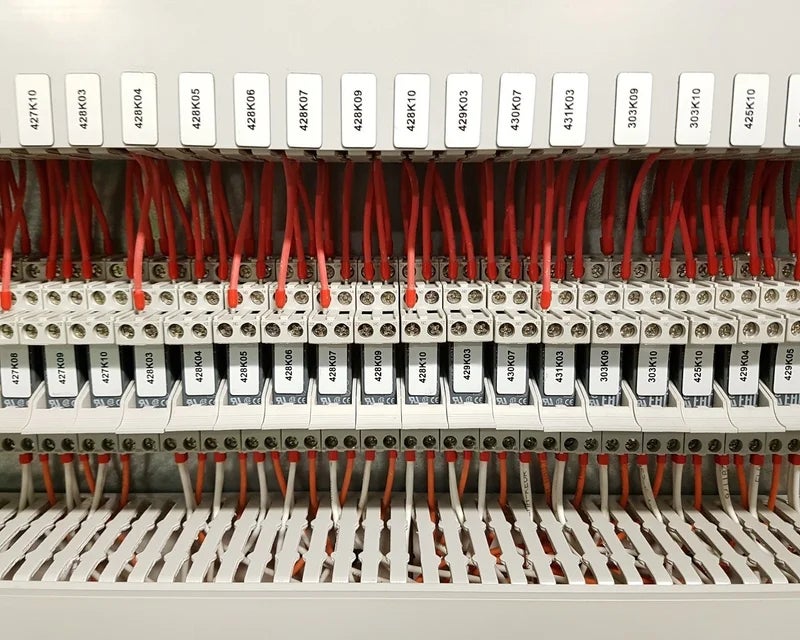 Witte ResoPrint labels met componentcodes op relais bij klemmenstroken in schakelkast, als duurzaam alternatief voor resopal labels