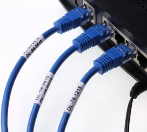 Witte wikkellabels met identificatiecodes op blauwe netwerkkabels aangesloten op netwerkswitch voor kabelcodering