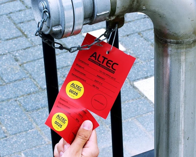 Rode industriële tag met controlestrook bevestigd aan een leiding voor inspectie en registratie