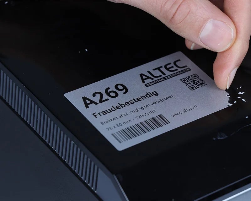 Hand probeert fraudebestendig vinyl label van elektronisch apparaat te verwijderen waarbij het label afbrokkelt