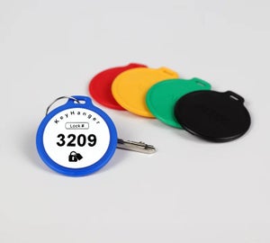 Blauwe KeyHanger met unieke nummering bevestigd aan een sleutel met meerdere gekleurde sleutelhangers op de achtergrond
