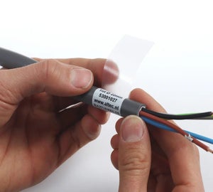 Handen die een transparant wikkellabel aanbrengen op grijze kabel met gekleurde aders