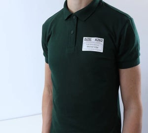 Verwijderbaar kledinglabel met naam en identificatiecode bevestigd op een groene polo