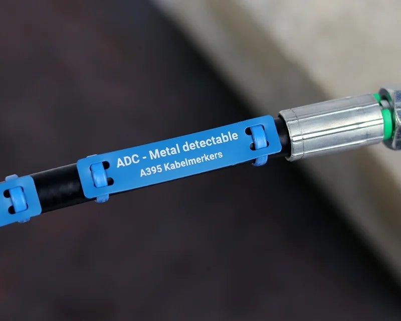 Blauwe metal detectable kabelmerker bevestigd rond een industriële kabel met bedrukte identificatie