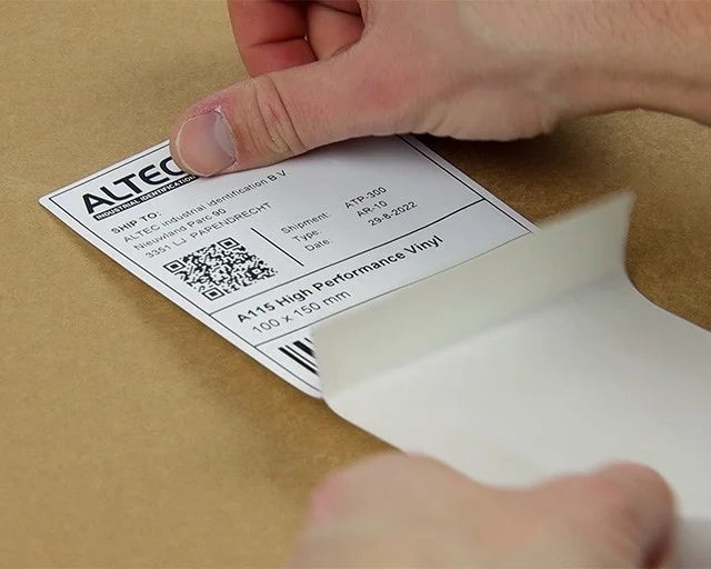 Geprint vinyl verzendlabel met adresgegevens, barcode en datamatrixcode wordt van de drager verwijderd