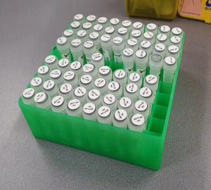 Groene cryobox gevuld met tientallen transparante laboratoriumbuisjes waarvan de doppen zijn voorzien van ronde witte cryogene labels met zwarte tekst