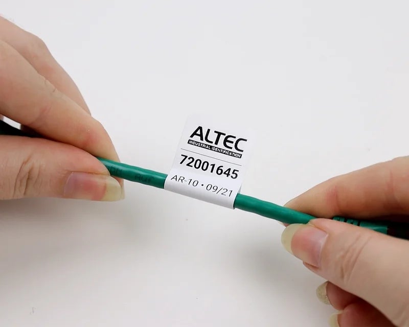 Handen die een kabelvlag met serienummer aanbrengen op groene kabel