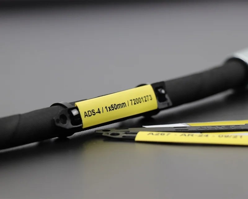 Zwarte draagstrip gemonteerd op een kabel met een gele ADS-4 krimpkous waarop een unieke codering is bedrukt