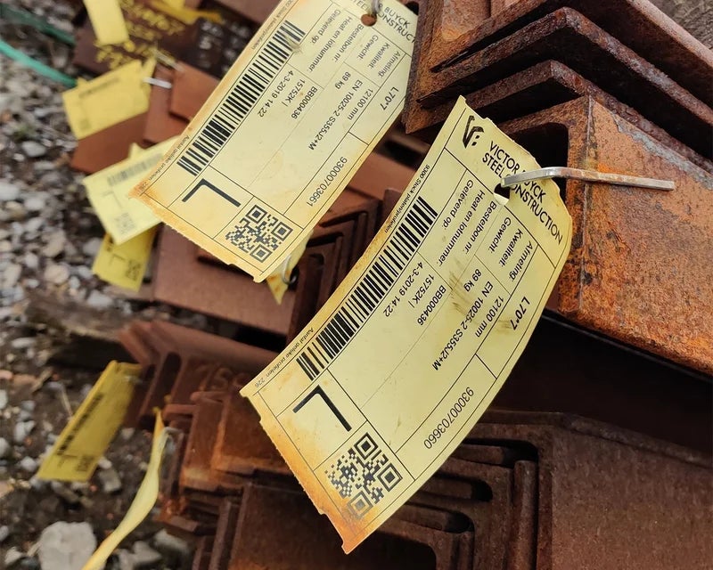 Gele industriële tags met barcode bevestigd aan roestige staalprofielen buiten