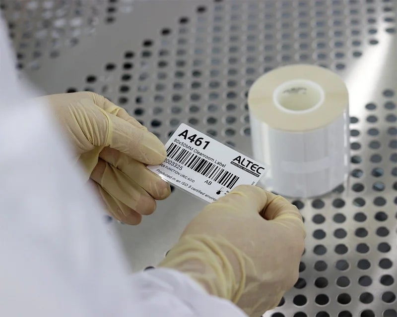 Handen houden een cleanroom label vast naast rollen labels in een steriele omgeving.