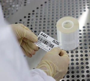 Handen houden een cleanroom label vast naast rollen labels in een steriele omgeving.