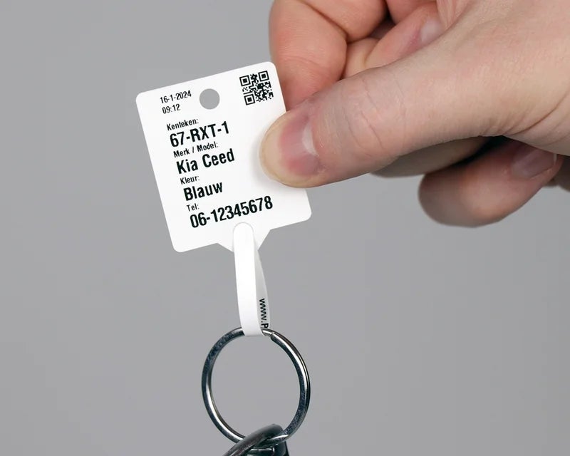 Wit sleutellabel met QR-code en voertuiggegevens vastgehouden