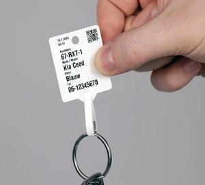 Wit sleutellabel met QR-code en voertuiggegevens vastgehouden