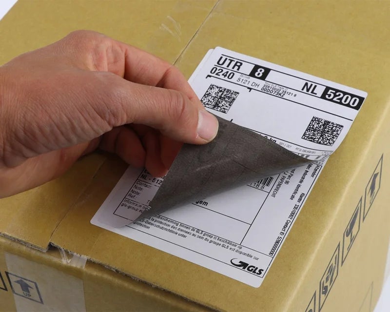 Correctielabel wordt over een bestaand verzendetiket op een kartonnen doos geplakt om onjuiste informatie af te dekken