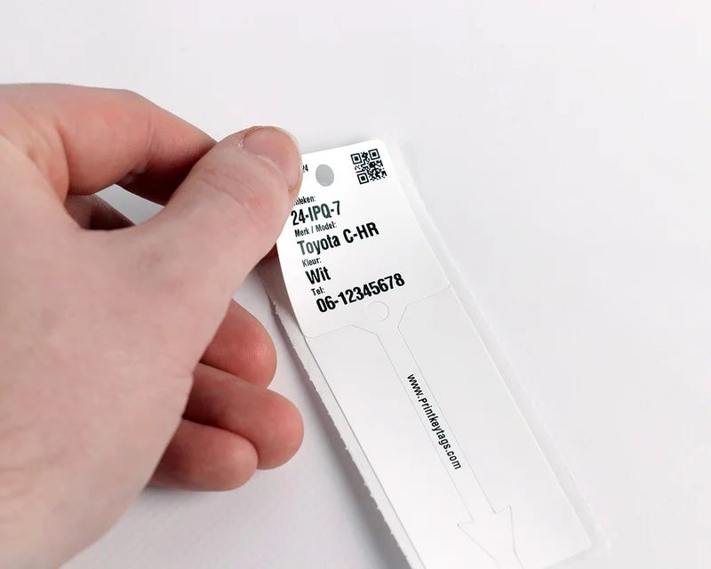 Witte KeyTag losgemaakt van drager met perforatie en bevestigingsstrip zichtbaar