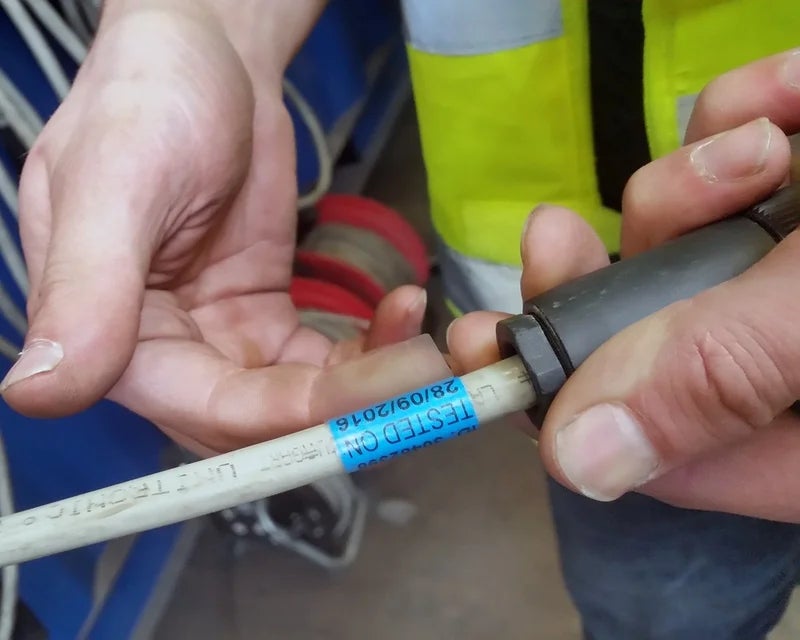 Blauw wikkellabel met testdatum op grijze kabel voor keuring in het veld