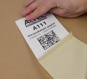 Geprint papieren verzendlabel met barcode en datamatrixcode wordt van de drager verwijderd