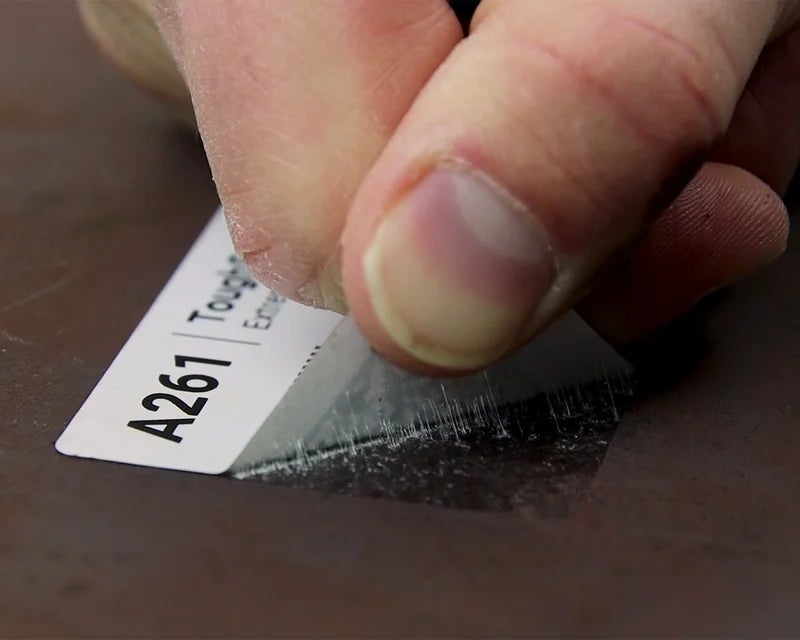 Hand probeert ToughSurface Extreme label van metalen oppervlak te verwijderen