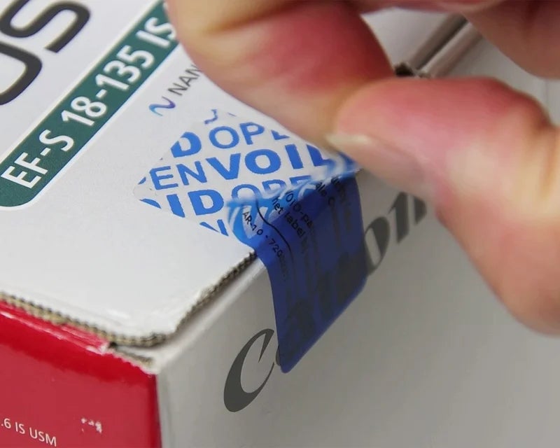 Security label met VOID-overdracht wordt losgetrokken van verzegelde kartonnen verpakking