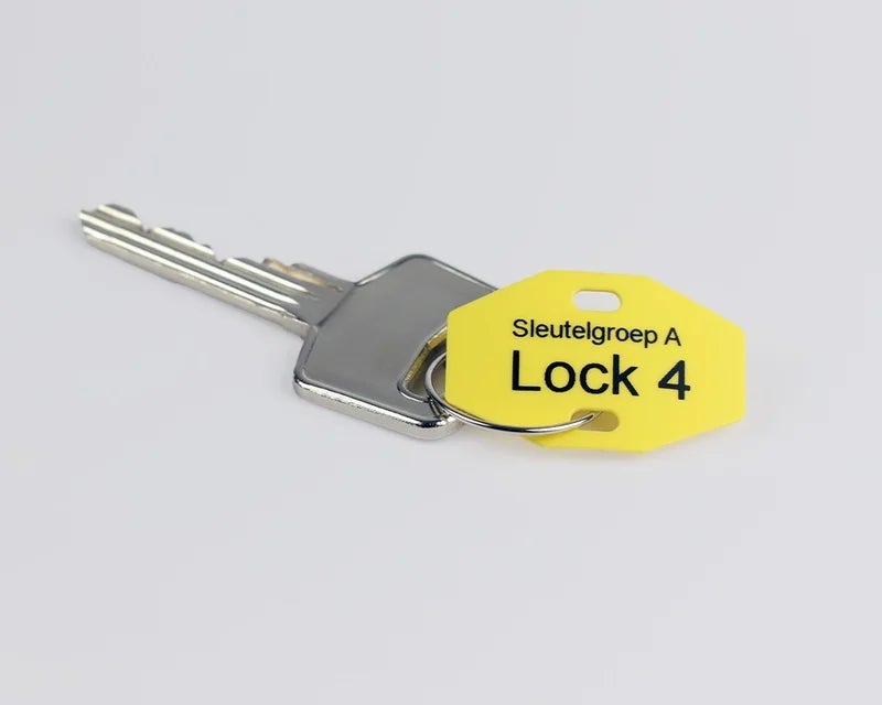 Geel sleutellabel met bedrukking bevestigd aan een metalen sleutel voor sleutelidentificatie
