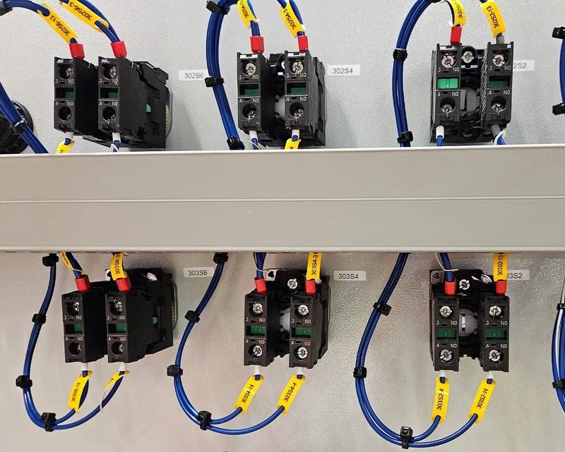 Gele wire tags met adercodes op blauwe aders bij componenten in schakelkast