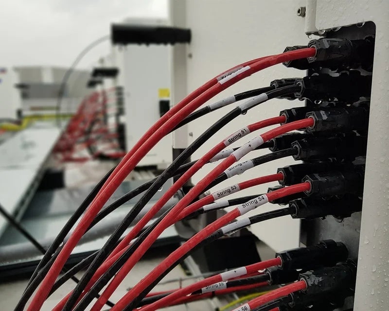 Witte wikkellabels met stringnummers op rode en zwarte PV-kabels bij zonne-energie installatie